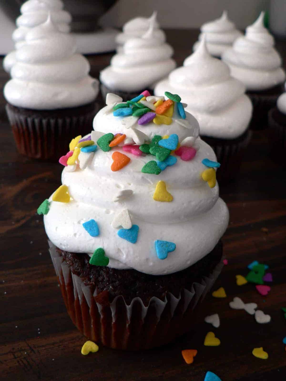 chocolate cupcake with white frosting and heart shaped sprinkles.