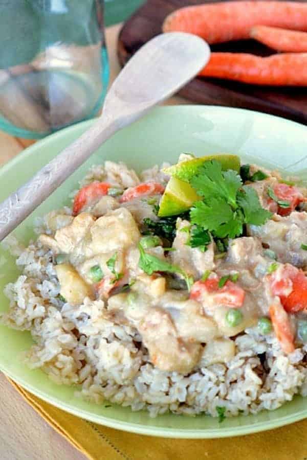 A bowl of chicken and vegetables in Thai Green Curry sauce over rice with fresh cilantro and a lime wedge