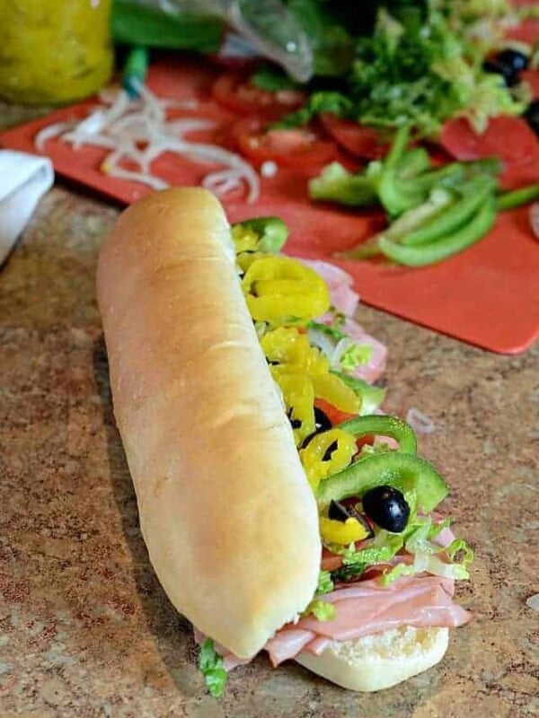long hoagie style sandwich with green peppers, black olives, meat hanging out.