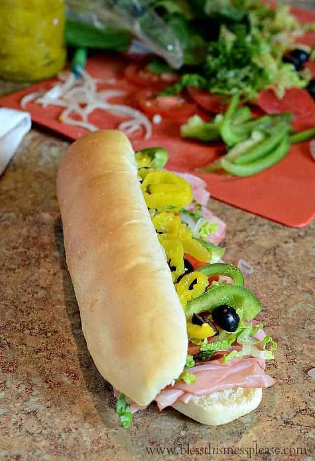 long hoagie style sandwich with green peppers, black olives, meat hanging out.