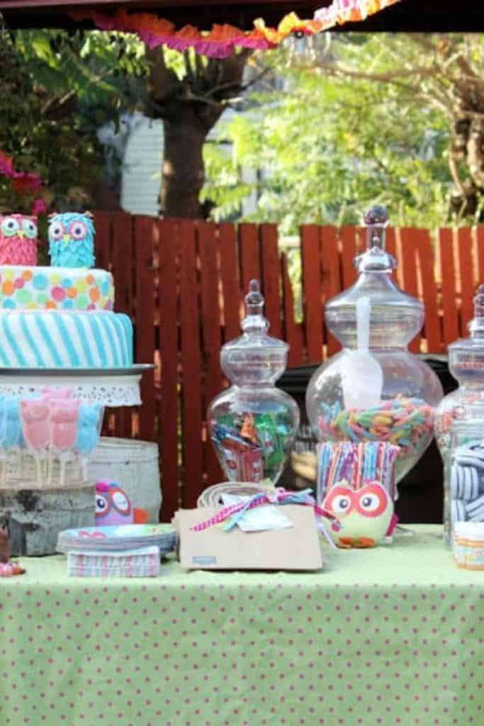 A party table with owl-themed decorations, cake, and jars of candy