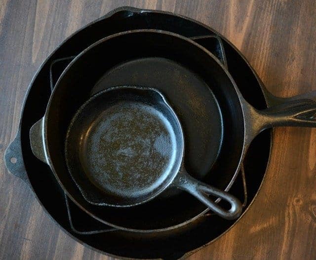 four black cast iron skillets nested together on a brown wood background.