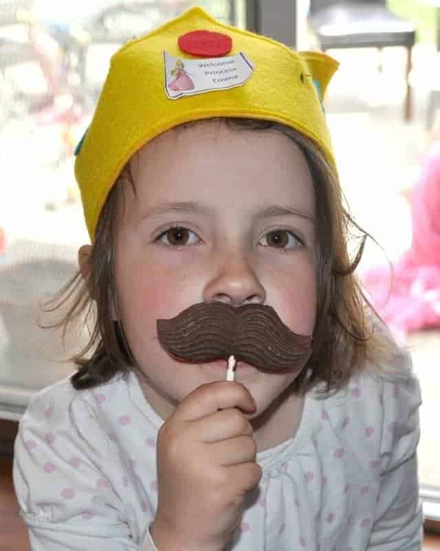 a girl with a chocolate mustache on a stick