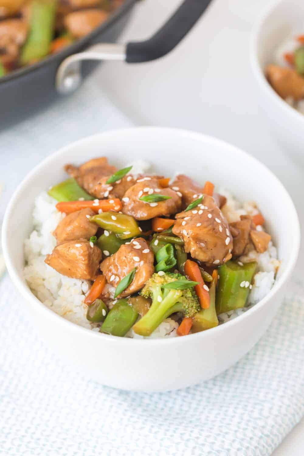 stir fry chicken and vegetables with white rice in a white bowl closeup