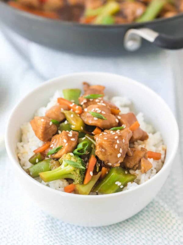 stir fried sticky saucy chicken and veggies in a pan and then the served on the side over rice in a white bowl