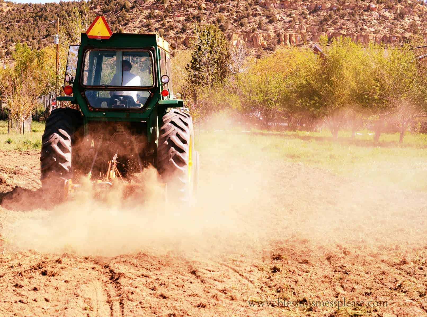 Image of a green tractor pulling an implement and creating dust.  