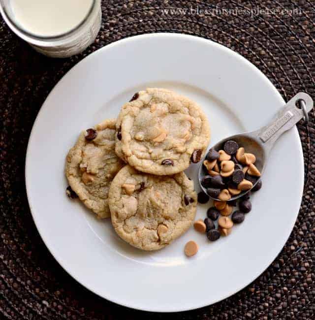 cookies on a plate with chocolate and peanut butter chips in a spoon and a glass of milk beside.