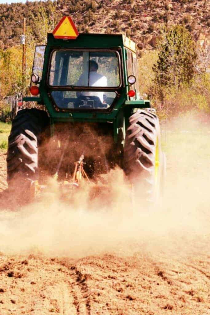 Rear-view of a green tractor plowing a dusty field