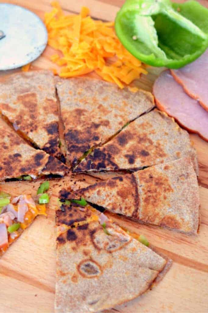 Ham and cheese quesadilla with diced green pepper cut into wedges on a wooden cutting board