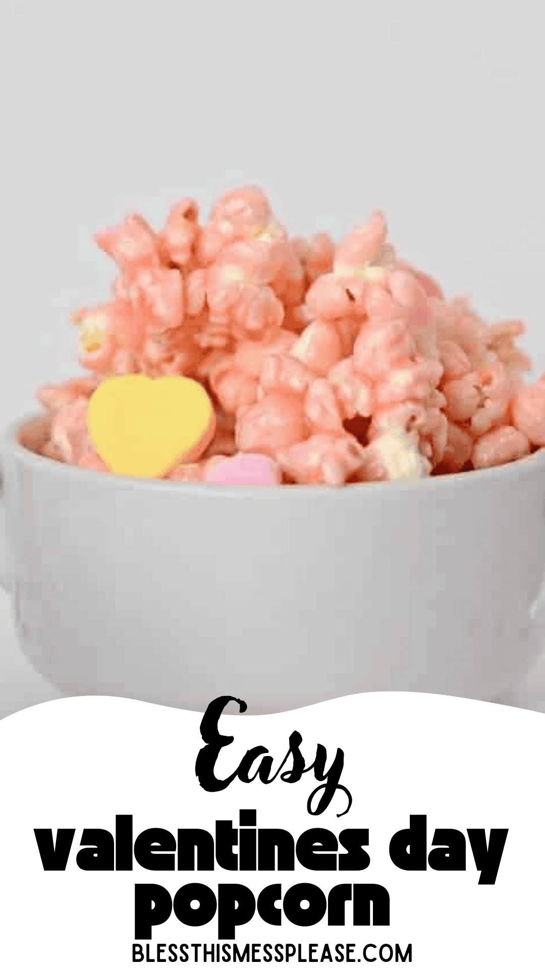 A white bowl filled with pink, candy-coated popcorn and heart-shaped candies makes the perfect valentine popcorn treat. Text on the image says, Easy valentines day popcorn BLESSTHISMESSPLEASE.COM.