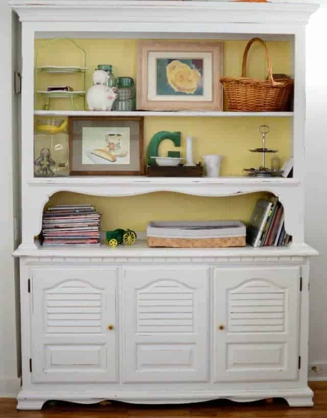 white furniture with shelves on top and drawers on bottom and various knick knacks like pictures and baskets on shelves.