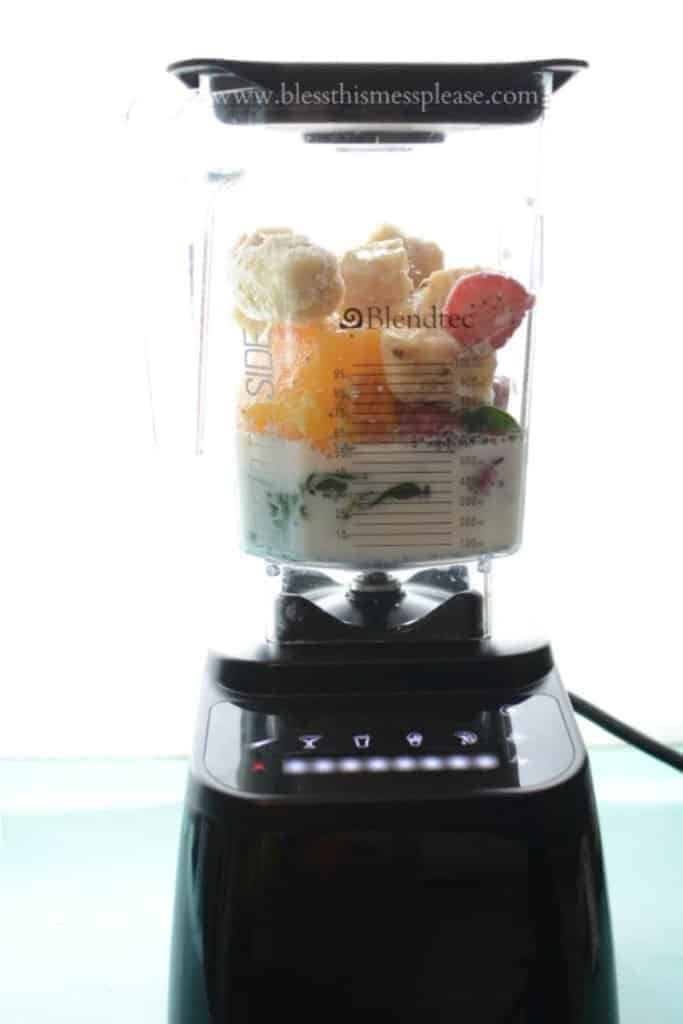 A blender filled with smoothie ingredients, including fruit, greens, and nut milk