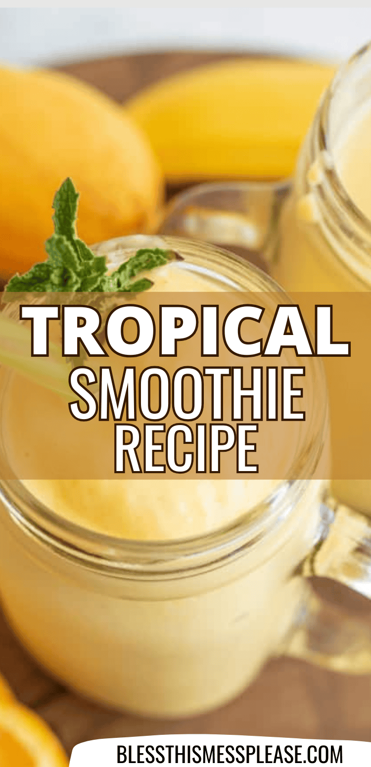Two glass mugs filled with creamy yellow tropical smoothies, garnished with mint and surrounded by fresh mangoes. Bold text across the image reads tropical smoothie recipe. Website blessthismessplease.com appears at the bottom.