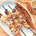 A white oval platter with Grilled Brown Sugar Bacon Wrapped Chicken Skewers and strips of bacon