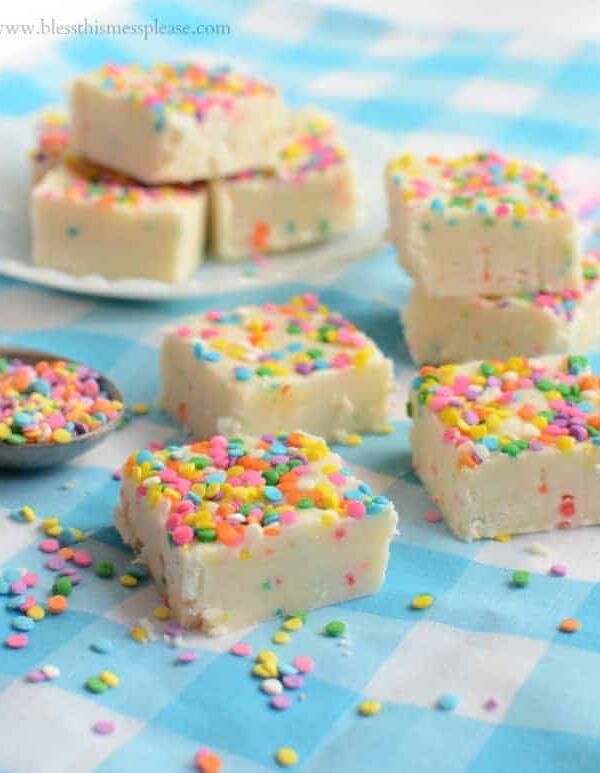 White fudge squares with rainbow sprinkles on a blue and white checked cloth
