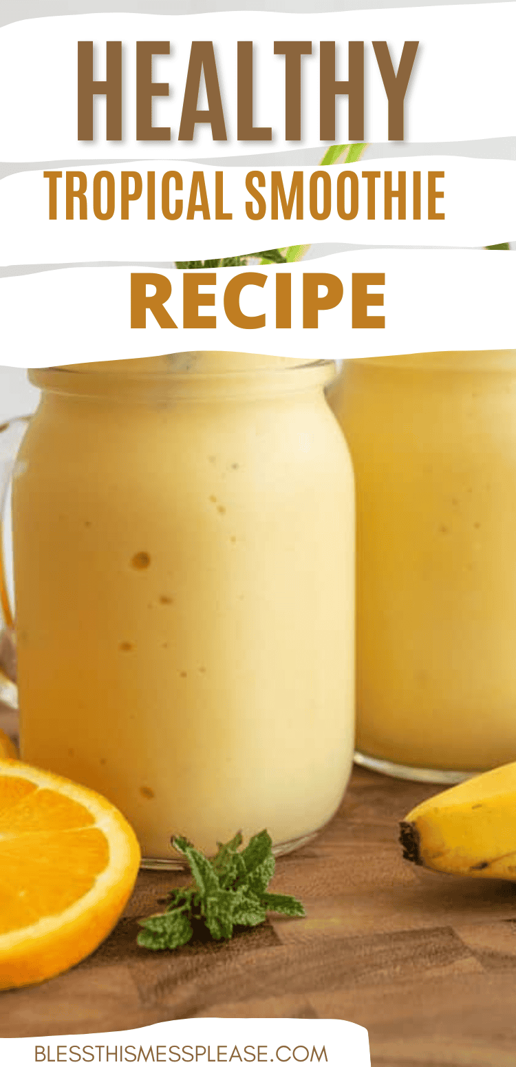 Two glass jars filled with creamy yellow smoothie sit on a wooden surface, surrounded by a sliced orange, whole banana, and mint. Text above reads, &ldquo;Healthy Tropical Smoothie Recipe&rdquo;&mdash;the perfect tropical smoothie recipe for any day.