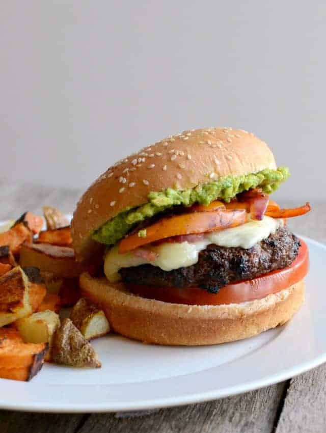 a burger with melted cheese, peppers, and guacamole