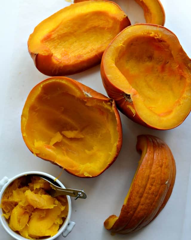 The best and easiest way to cook a pumpkin - tasty and cheaper than normal canned pumpkin! Top view of a slow cooked pumpkin on a counter with the innards being scooped into a bowl.