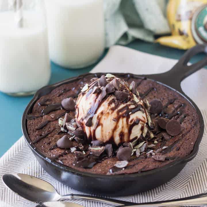 a brownie sundae in a miniature cast iron skillet with a spoon and a glass of milk to the side