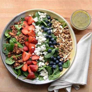 Bowl of berry spinach salad with a cup of citrus poppy seed dressing
