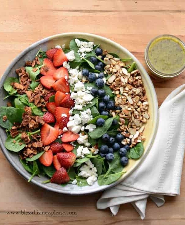 Bowl of berry spinach salad with a cup of citrus poppy seed dressing