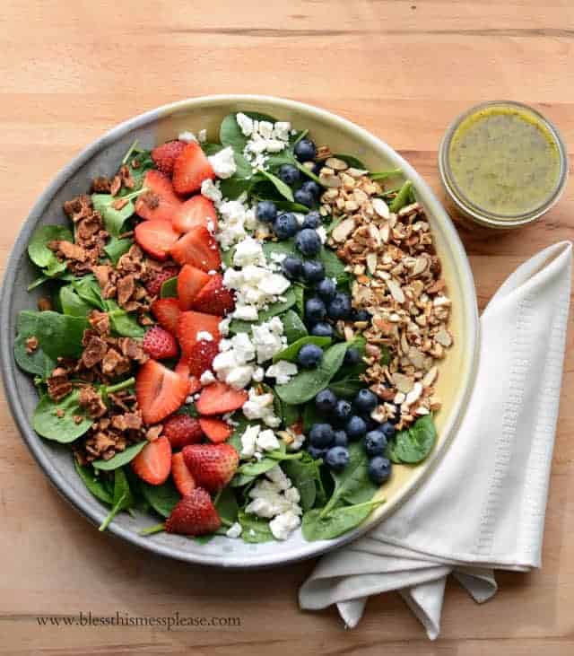 Bowl of berry spinach salad with a cup of citrus poppy seed dressing