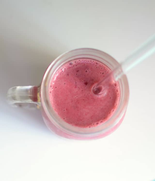 cherry smoothie in a glass mug with a large straw inserted