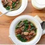 Top view of slow cooker sausage and bean soup with greens in a white bowl