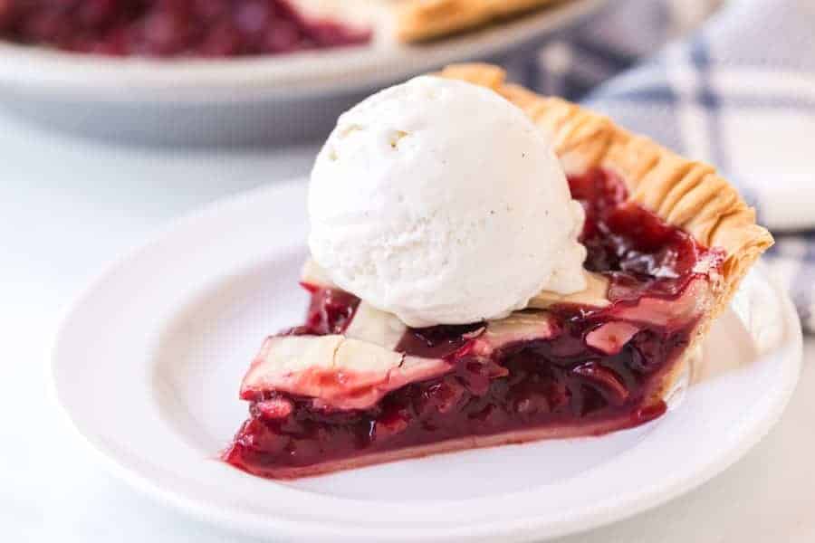 slice of cherry pie with scoop of vanilla ice cream on round white plate