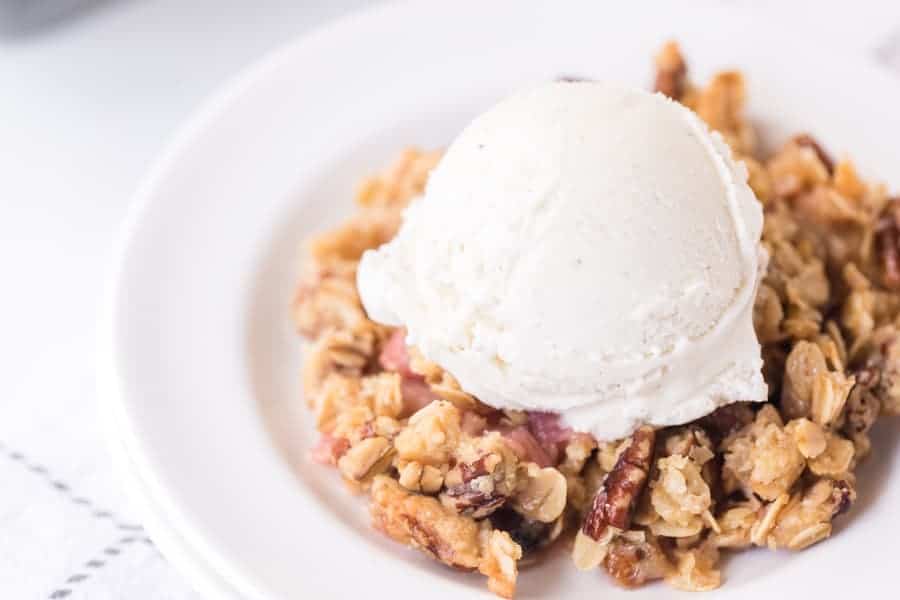 closeup shot of rhubarb crisp on round white plate with scoop of vanilla ice cream