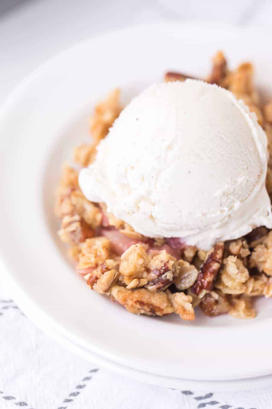 closeup of rhubarb crisp in white bowl with scoop of vanilla ice cream