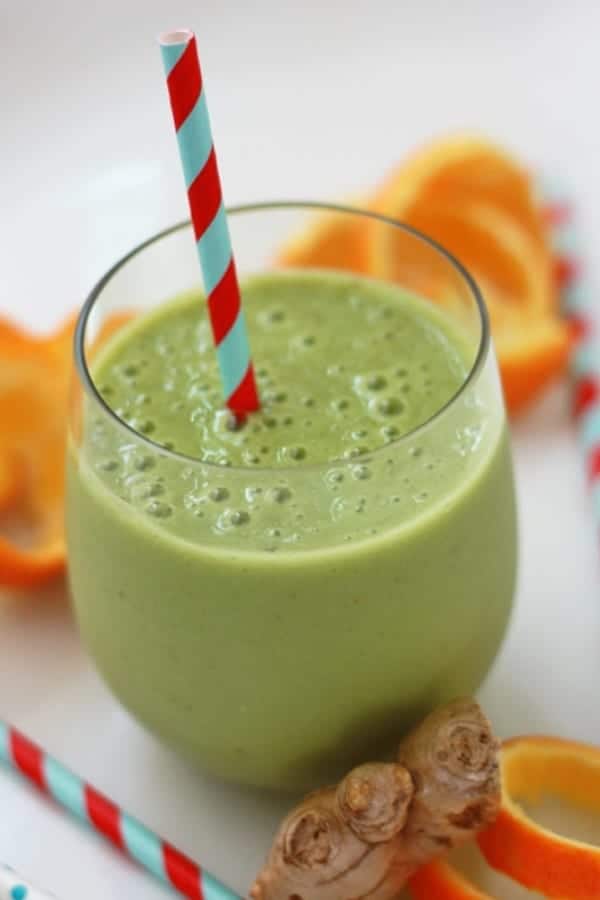 A clear glass of green smoothie with a striped straw