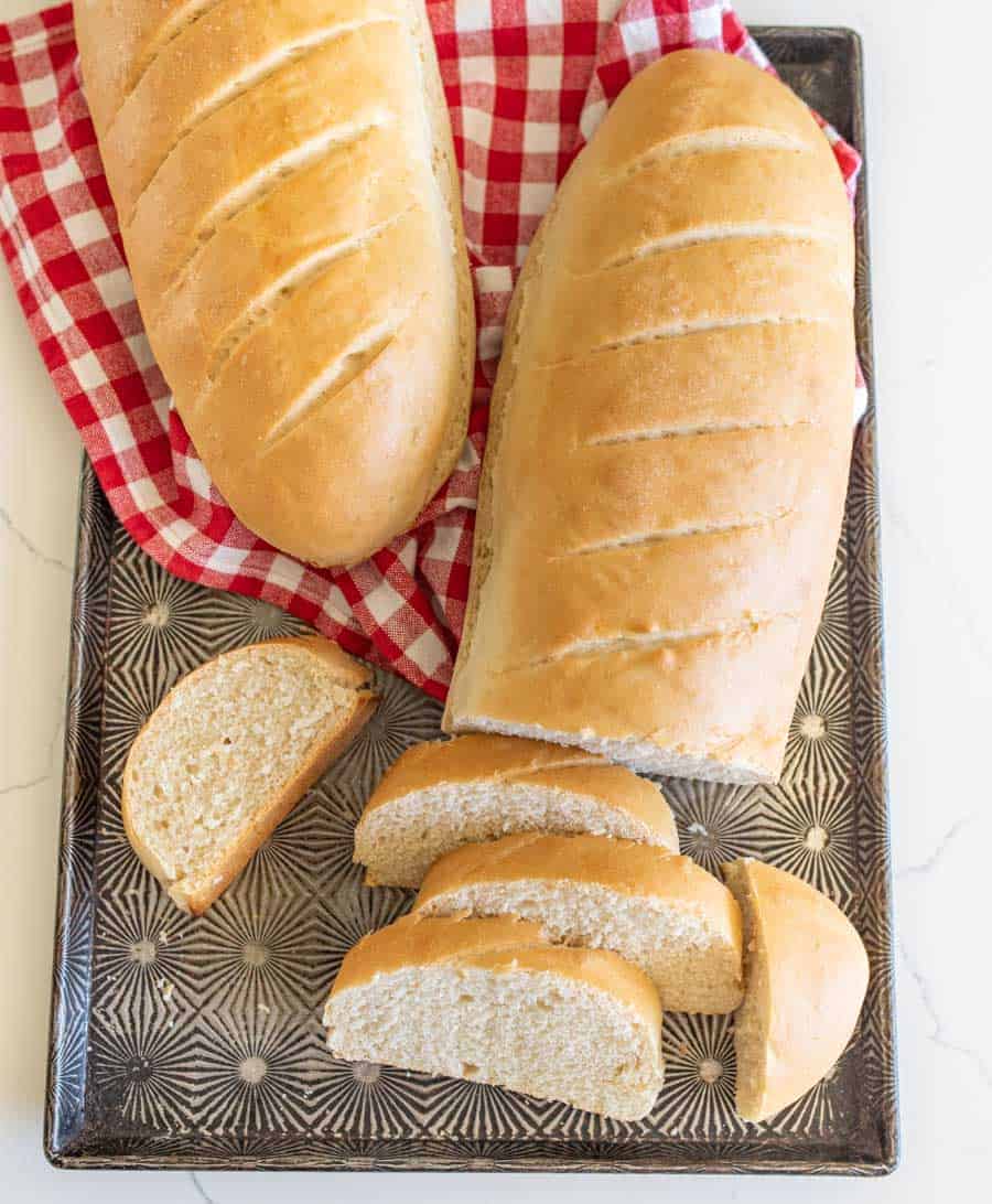 two loaves of french bread with slices of bread on tray with red checkered towel