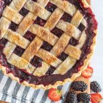 picture of triple berry pie on a wood board with fresh berries in front