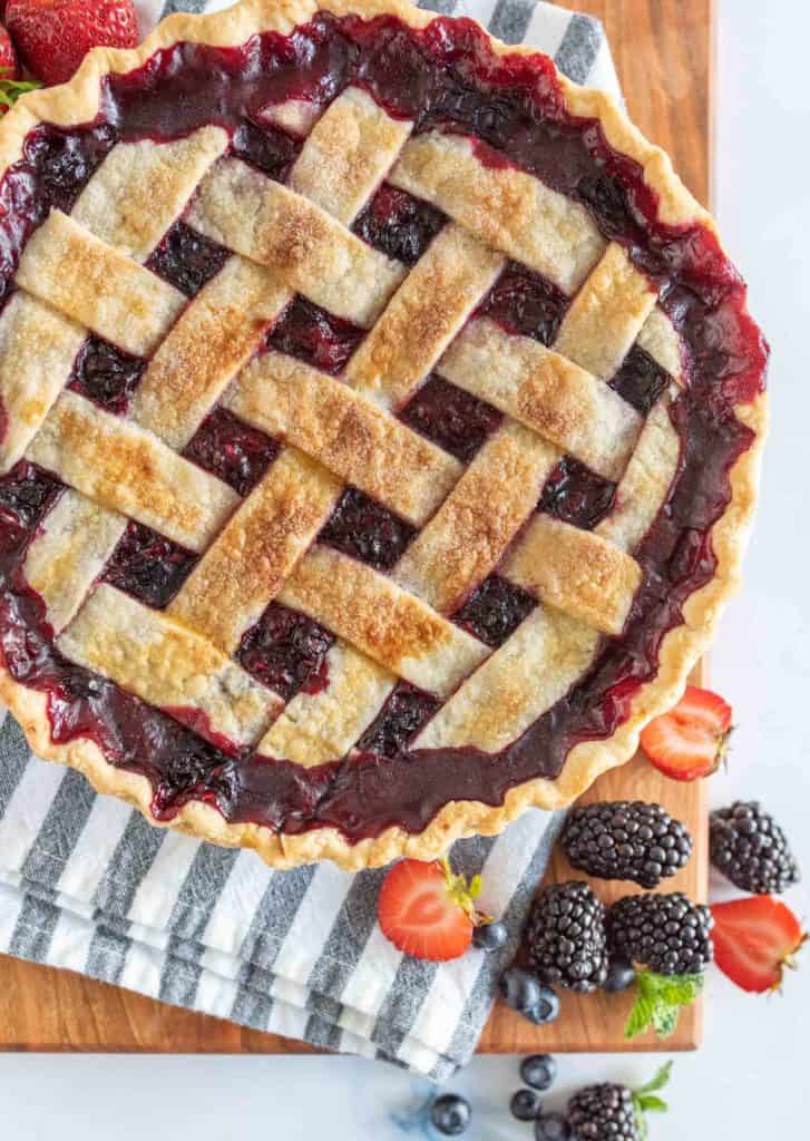picture of triple berry pie on a wood board with fresh berries in front
