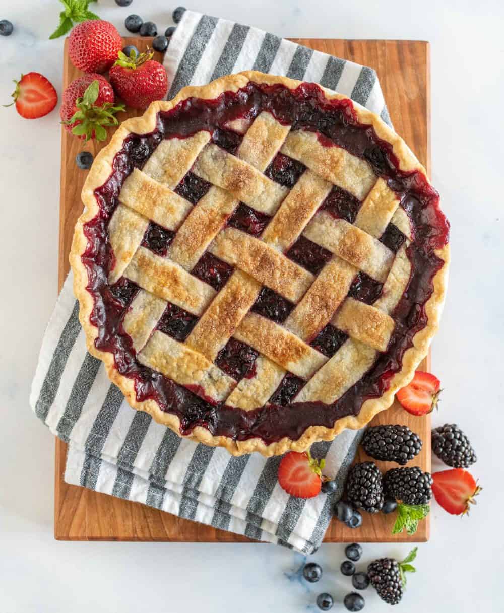 picture of triple berry pie on a wood board with fresh berries in front