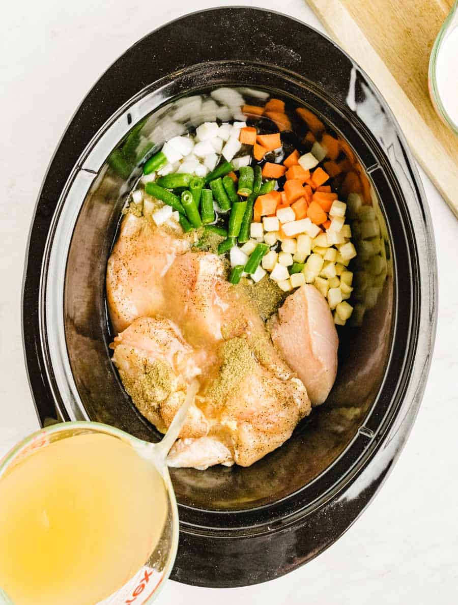 ingredients for slow cooker chicken pot pie in a slow cooker with broth being poured into it