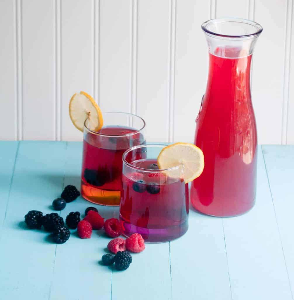 A carafe and two glasses of berry lemonade with fresh berries and lemon slices