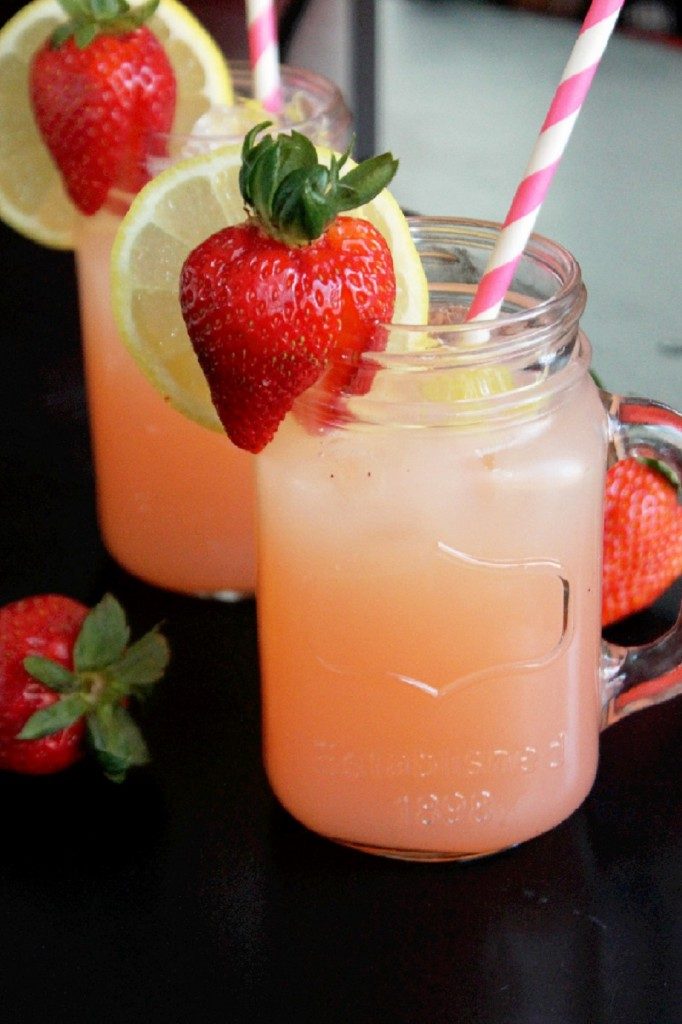 A mason jar of strawberry lemonade with fresh strawberry, lemon slice, and a straw