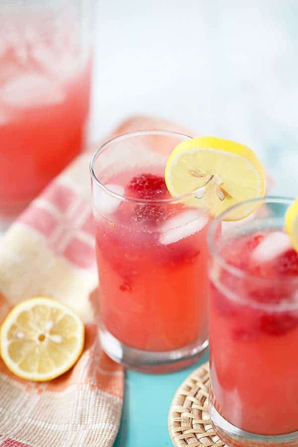 Two glasses of raspberry lemonade with fresh raspberries and a lemon slice