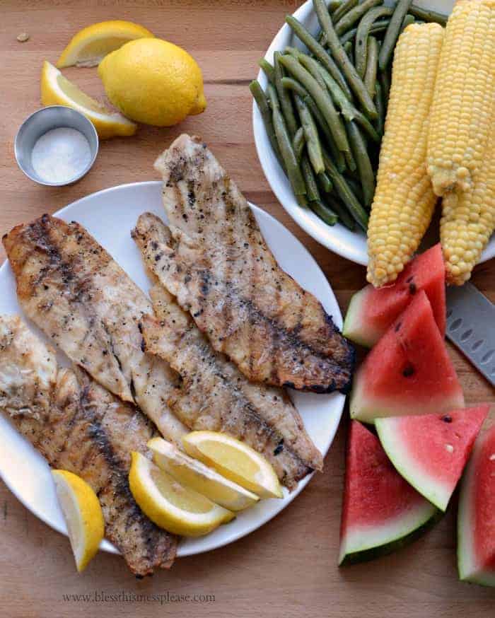 White fish fillets with grill marks, served with salt, lemon, and sides.