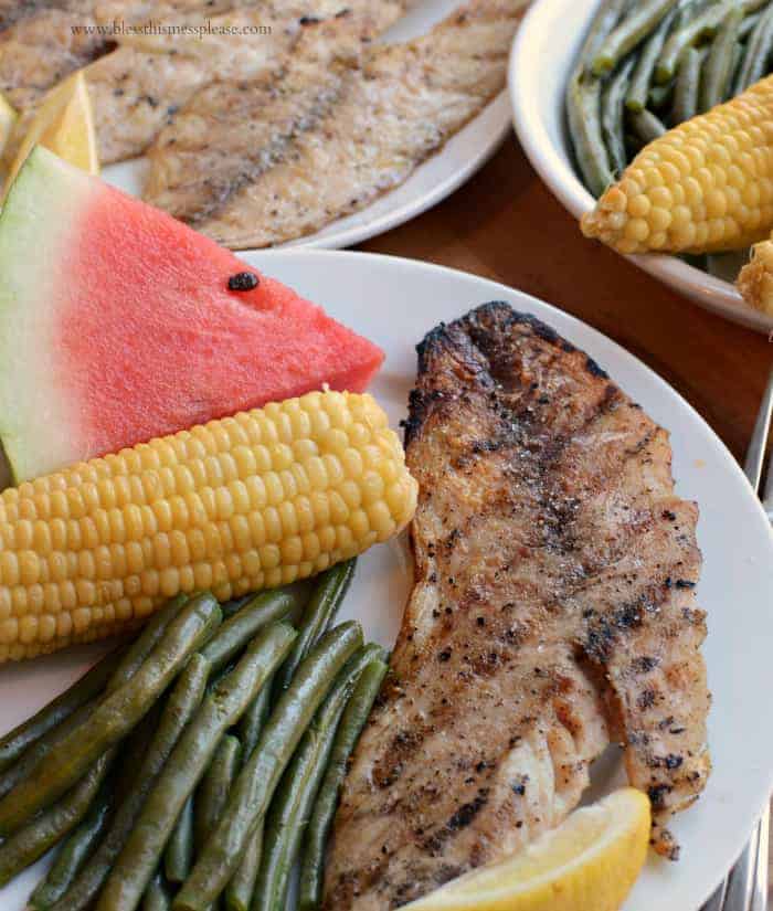 Grilled fish fillet served on plate with corn on the cob, green beans, and watermelon.