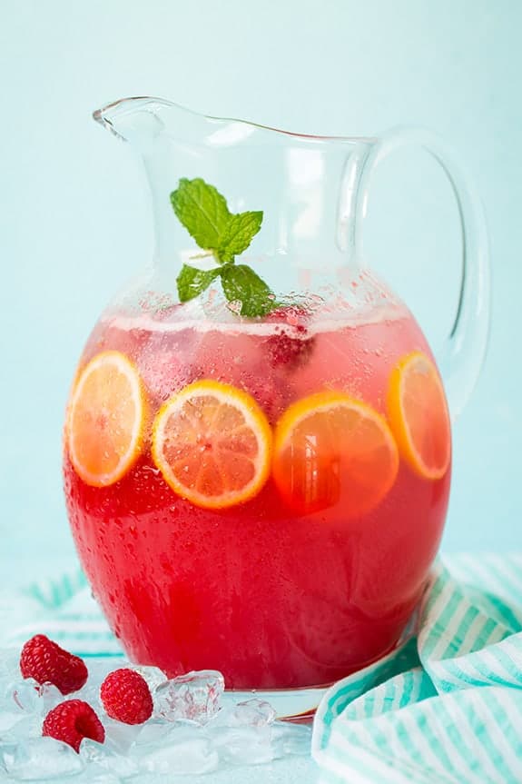A pitcher of sparkling raspberry lemonade with lemon slices, fresh raspberries and a mint leaves