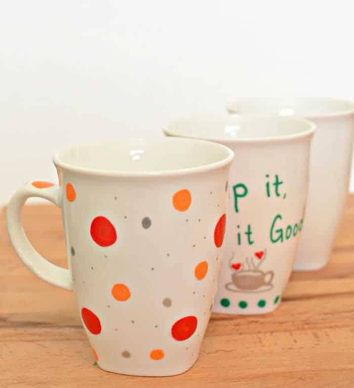 Painted Sharpie Mugs (that won't wash off!) Three painted sharpie mugs in a diagonal line on a wooden counter.