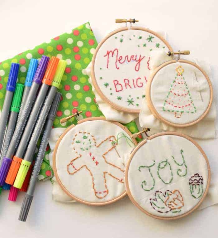 Simple Embroidered Ornaments Four simple embroidered Christmas ornaments in hoops before finishing next to some green and red fabric and some washable fabric markers.