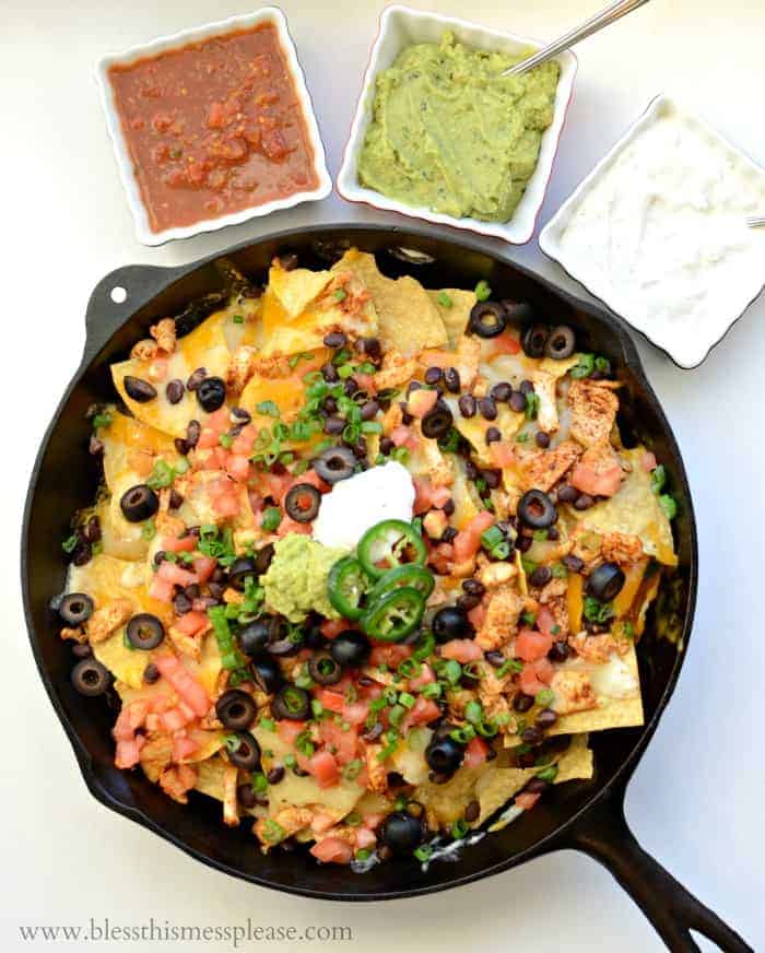 a skillet of nachos with guacamole, salsa, and sour cream in small dishes to the side