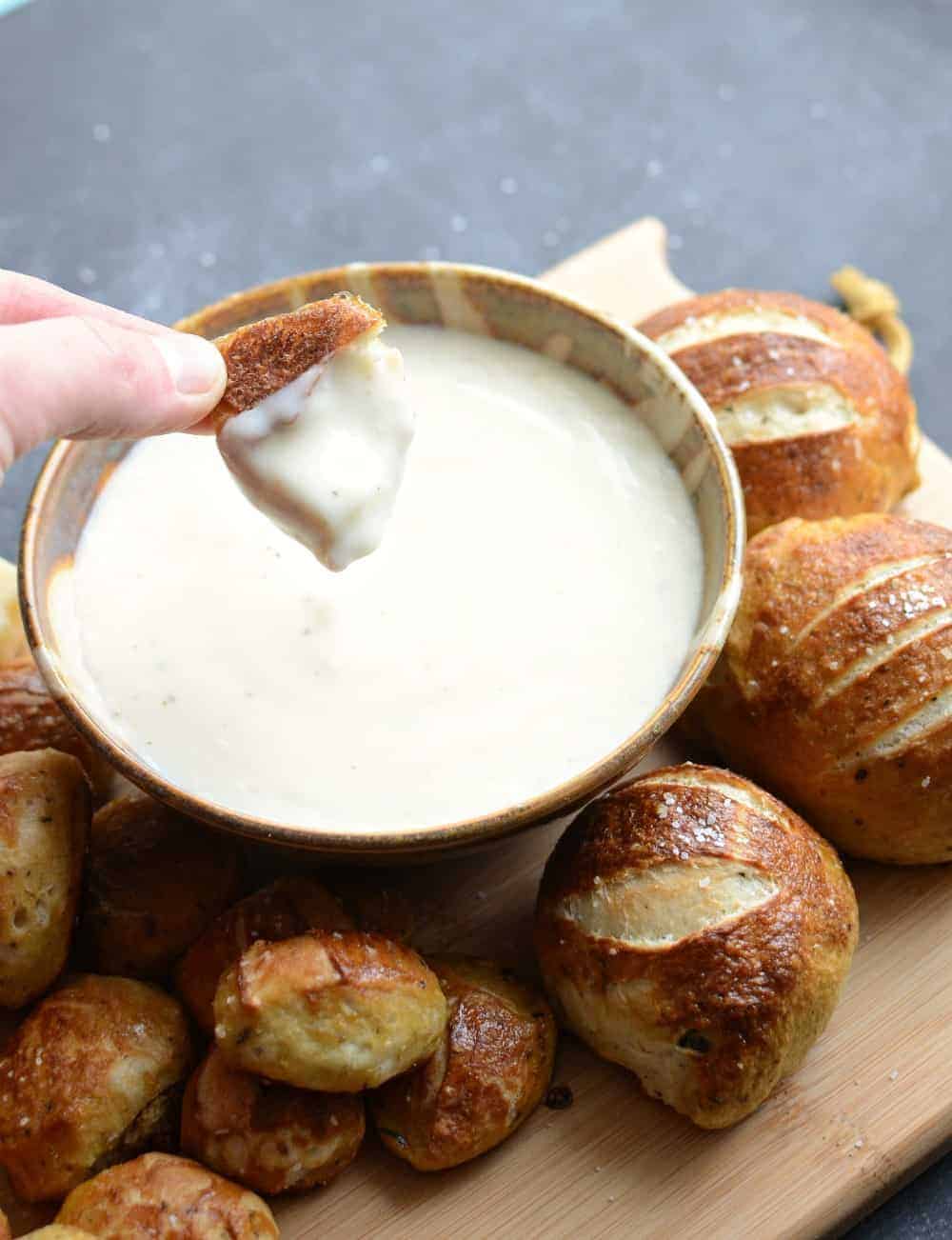 A close-up of the baked parmesan pretzel bites on a bamboo cutting board with a bowl of the parmesan dipping sauce. 