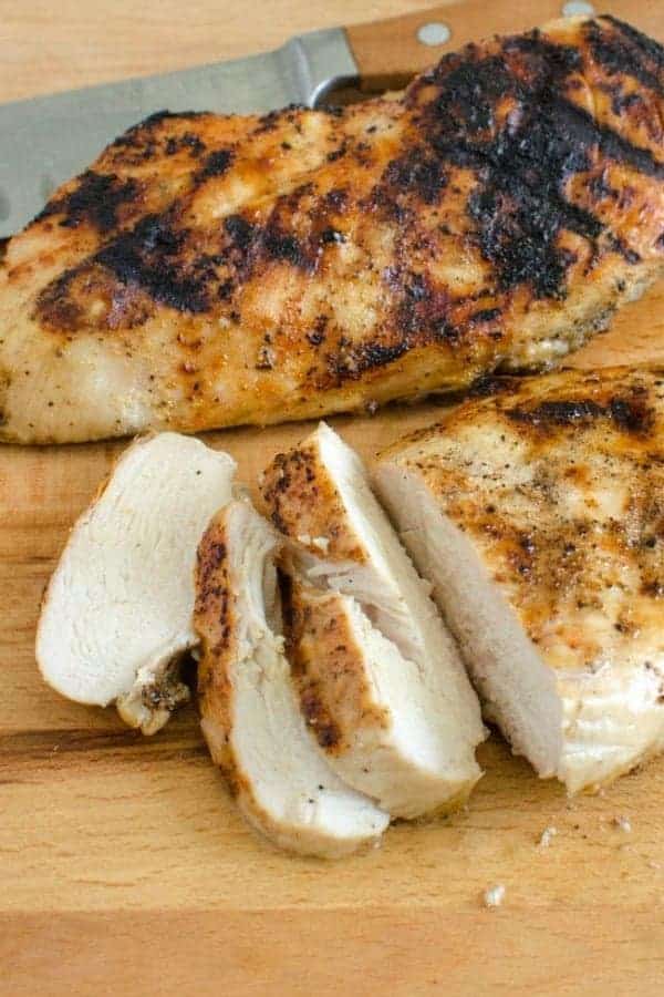 Grilled seasoned whole chicken breast on a cutting board with a few sliced pieces
