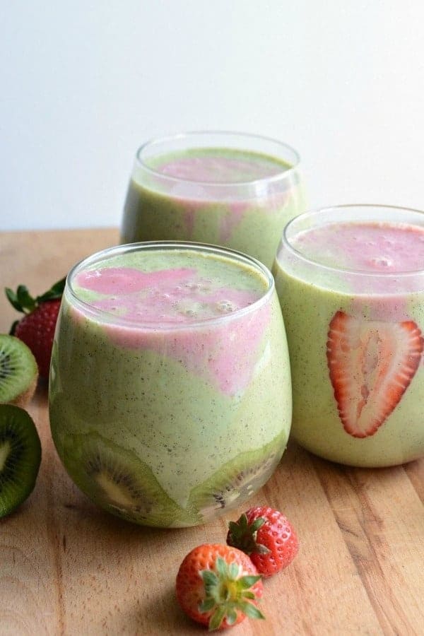 Strawberry kiwi smoothies in clear glasses with green and pink swirls and slices of fresh strawberries and kiwi