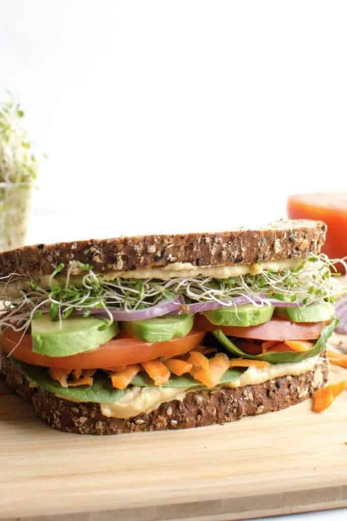 hummus and veggie sandwich with sprouts on sliced wheat bread